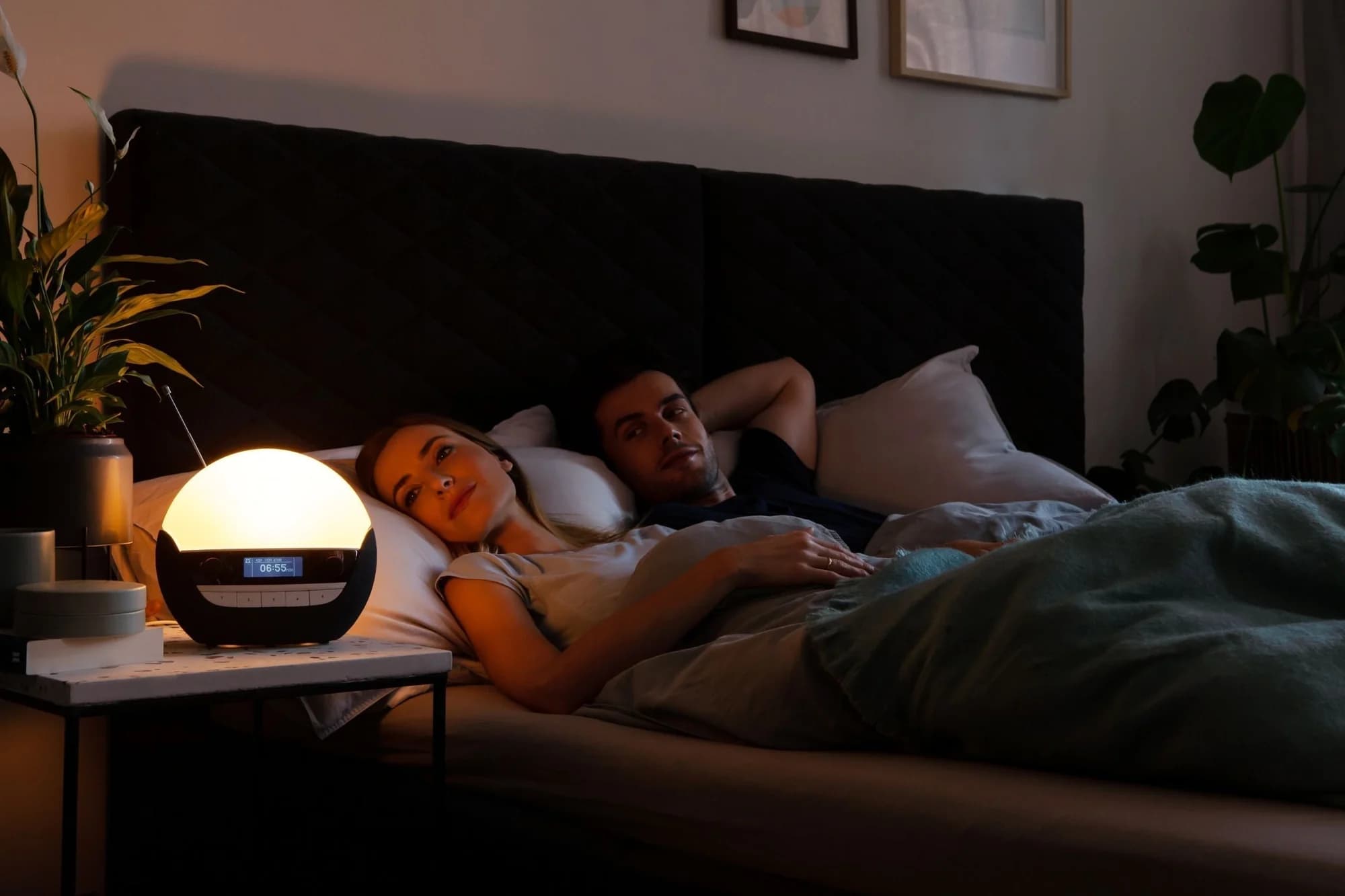 Der Lichtwecker Lumie 750 Luxe DAB leuchtet warm auf dem Nachttisch, daneben ein Paar im Bett